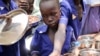 Children push their plates out to receive a portion of cooked grains during a lunchtime feeding program initiative by UNICEF and WFP with the aim of providing daily meals to 75,000 children in Aweil, N. Bahr el Ghazal state, S. Sudan, March 26, 2019.