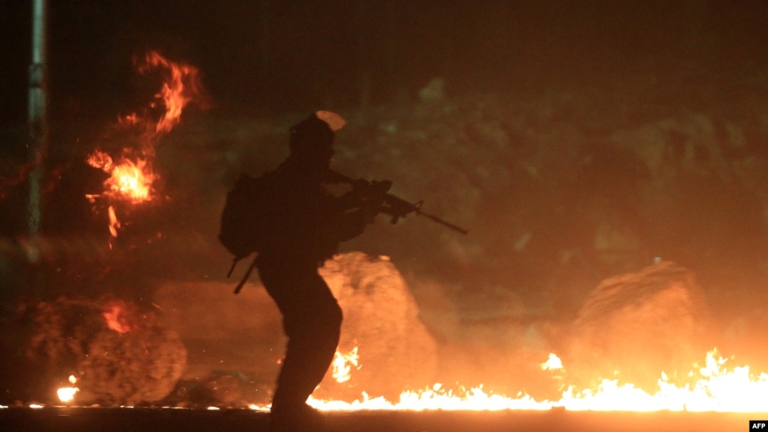 Seorang petugas keamanan Israel melewati ban-ban yang dibakar dalam demonstrasi sekitar 10.000 warga Palestina yang memprotes serangan militer Israel di Gaza, di antara Yerusalem dan Ramallah (25/7). (AFP/Abbas Momani)
