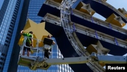 FILE - Workers dismantle the large euro sign sculpture for maintenance, in front of the headquarters of the former European Central Bank (ECB) in Frankfurt, July 6, 2015. 