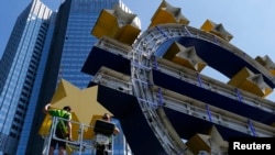 Workers dismantle the large euro sign sculpture for maintenance, in front of the headquarters of the former European Central Bank (ECB) in Frankfurt, July 6, 2015. 