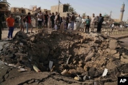 Civilians inspect a crater caused by a suicide car bombing at a busy market in Khan Bani Saad in the Diyala province, about 30 kilomters (20 miles) northeast of Baghdad, Iraq, July 18, 2015.