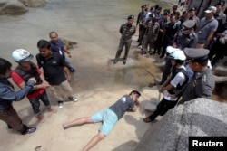 FILE - Two workers from Myanmar (wearing helmets and handcuffs), suspected of killing two British tourists on the island of Koh Tao, stand near Thai police officers during a re-enactment of the alleged crime, where the bodies of the tourists were found.