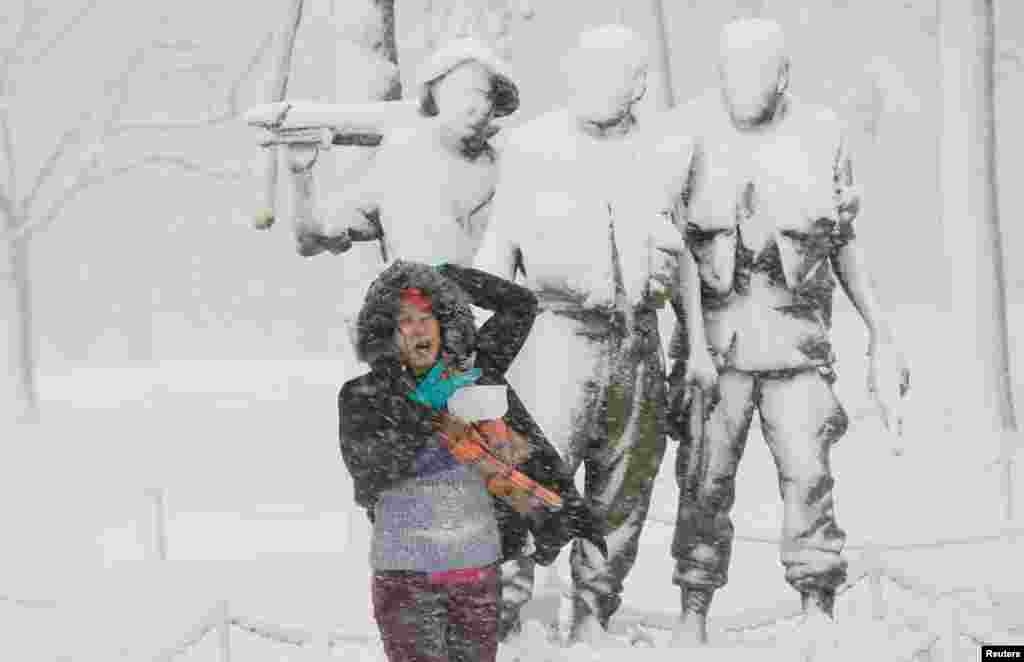 Una mujer posa para una fotografía debajo de una estatua cubierta de nieve en el Monumento a los Veteranos de Vietnam en el National Mall, en Washington DC.