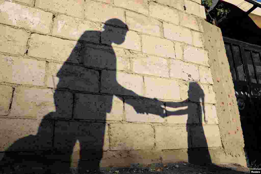 The shadow of a girl receiving a meal for Iftar, or the evening meal, to break fast during Ramadan, from a member of the "Tkiyet Um Ali" humanitarian services center is cast on a wall in front of her family home in the city of Russeifa, Jordan.