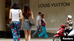 Women walk next to a Louis Vuitton sign as they enter the luxury Trang Tien Plaza shopping mall in Hanoi July 19, 2013. Picture taken July 19, 2013. To match Feature VIETNAM-CONSUMERS/ REUTERS/Kham (VIETNAM - Tags: BUSINESS LOGO) - RTX12AIU