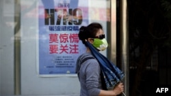 Phụ nữ đeo mặt nạ đi ngang một áp phích hướng dẫn cách làm thế nào để tránh virus cúm gia cầm H7N9 trên đường phố ở Bắc Kinh.