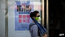 A woman wears a face mask as she walks past a poster showing how to avoid the H7N9 avian influenza virus, by a road in Beijing, April 24, 2013.