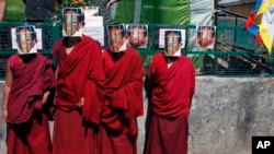 FILE - Exiled Tibetan Buddhist monks wear masks depicting Gendun Choekyi Nyima, the 11th Panchen Lama, behind bars to mark his 21st birthday in Dharmsala, India, April 25, 2010.