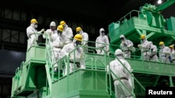 Members of the media and Tokyo Electric Power Co. (TEPCO) employees wearing protective suits and masks walk down the steps of a fuel handling machine on the spent fuel pool inside the No.4 reactor building at the tsunami-crippled TEPCO's Fukushima Daiichi