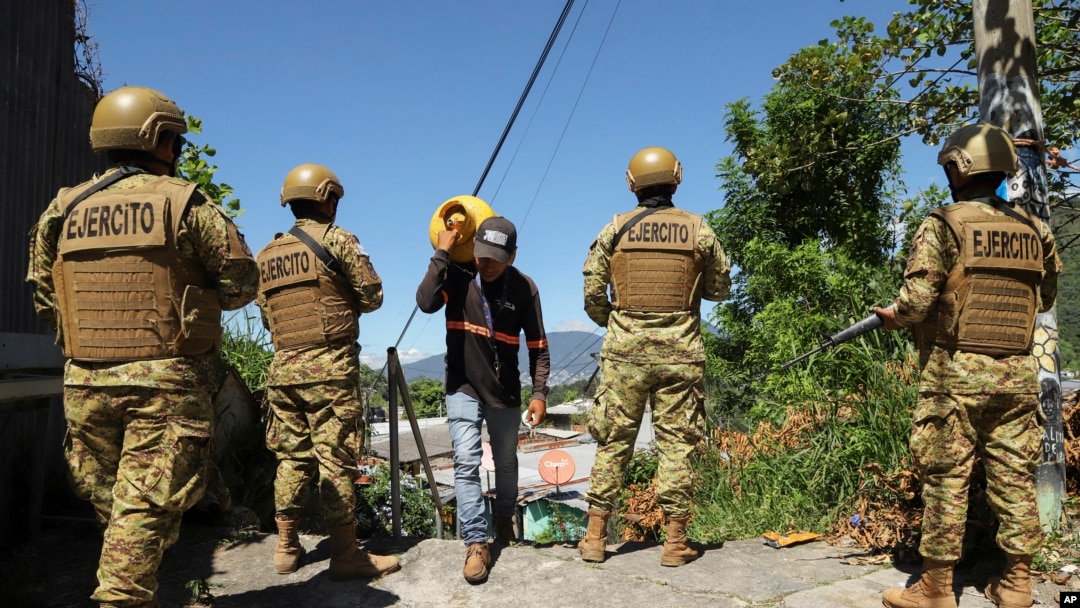ARCHIVO - Un hombre carga propano junto a soldados en el barrio 10 de Octubre durante un despliegue gubernamental de soldados y policías para reprimir las pandillas en San Marcos, El Salvador, el 28 de octubre de 2024. AP