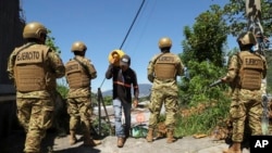 ARCHIVO - Un hombre carga propano junto a soldados en el barrio 10 de Octubre durante un despliegue gubernamental de soldados y policías para reprimir las pandillas en San Marcos, El Salvador, el 28 de octubre de 2024. AP