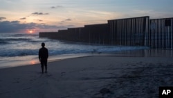 A man who gave his name as Hugo stands on the shore of the Pacific Ocean as his friend films him, backdropped by the U.S.-Mexico border fence that separates Tijuana, Mexico, from San Diego, California, April 4, 2017.