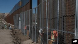 Para pekerja terus membangun pagar yang lebih tinggi di perbatasan yang memisahkan kota Anapra di Meksiko dan Sunland Park, New Mexico (25/1). (AP/Christian Torres)
