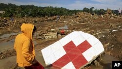 A woman stands next to a Red Cross sign among debris in a village hit by flashfloods brought by Typhoon Washi in Cagayan de Oro, southern Philippines, December 18, 2011.