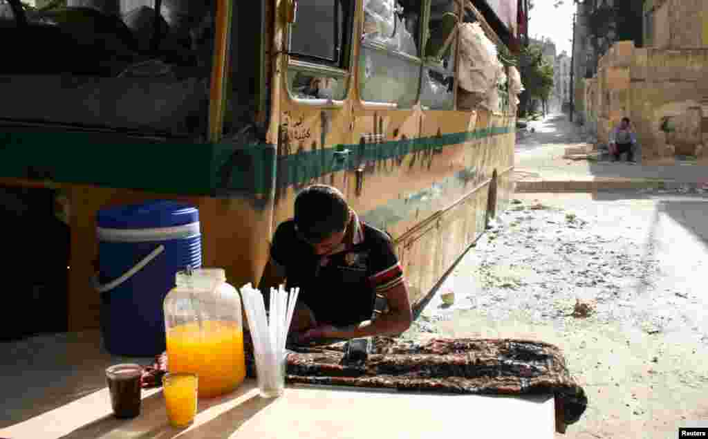 A boy sells juice near a damaged bus in Aleppo's Bustan al-Qasr neighborhood, May 30, 2013. 