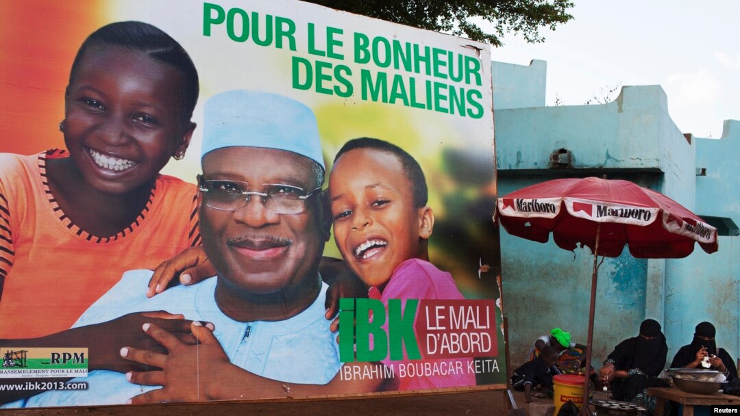 Women sell food in front of a poster for presidential candidate Ibrahim Boubacar Keita in Bamako, July 16, 2013. The poster reads, "For the happiness of Mali." 
