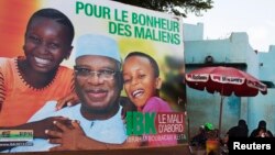 Women sell food in front of a poster for presidential candidate Ibrahim Boubacar Keita in Bamako, July 16, 2013. The poster reads, "For the happiness of Mali." 