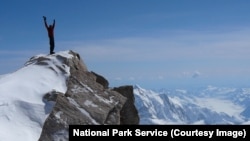 A mountaineer stands atop a tall peak in Denali National Park