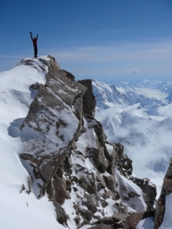 A mountaineer stands atop a tall peak in Denali National Park