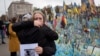 People react during a nationwide minute of silence in memory of fallen soldiers who defended their homeland in war with Russia, on Defenders Day at the improvised war memorial in Independence square in Kyiv, Ukraine, Oct. 1, 2024. 