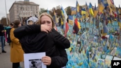 People react during a nationwide minute of silence in memory of fallen soldiers who defended their homeland in war with Russia, on Defenders Day at the improvised war memorial in Independence square in Kyiv, Ukraine, Oct. 1, 2024. 