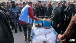 Pekerja Badan Bantuan dan Pekerjaan PBB untuk Pengungsi Palestina (UNRWA) membagikan jatah tepung dan pasokan lainnya kepada orang-orang di gudang UNRWA di Rafah di selatan Jalur Gaza pada 12 Desember 2023. (Foto: AFP)