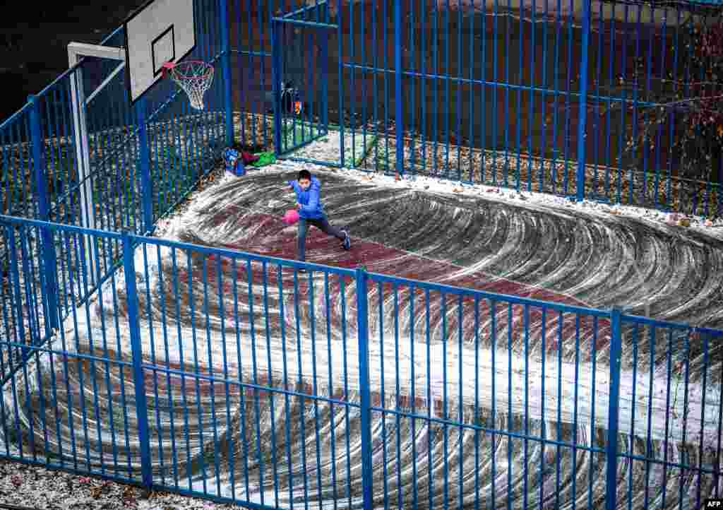 A schoolboy plays with a ball on a sports ground covered with a light layer of snow in Moscow, Russia.