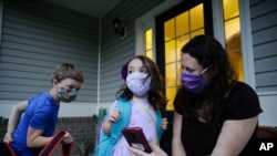 Rachel Adamus, right, shows her children, Paul, left, and Neva, 5, center, an app on her phone showing when the school bus will arrive near their home, on Aug. 3, 2020, in Dallas, Ga. 