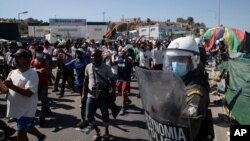 Asylum seekers take part in a rally as riot police block the road near Mytilene town, on the island of Lesbos, Greece, Sept. 11, 2020, after fires destroyed the notoriously overcrowded Moria camp, leaving thousands without shelter.