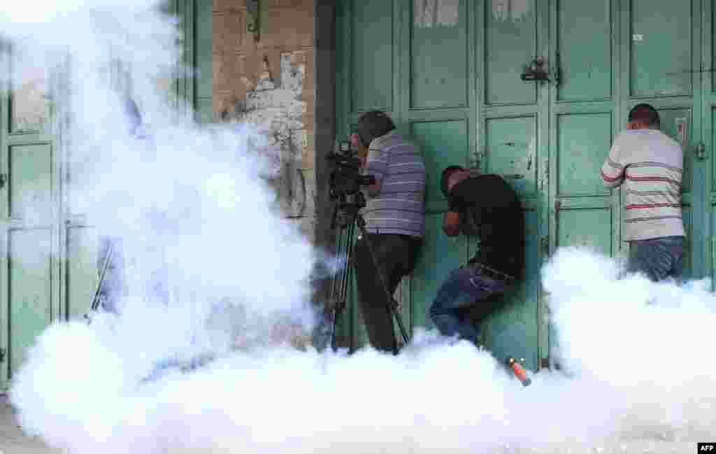 Palestinians take cover from tear gas and protect their ears from a sound grenade fired by Israeli security forces, during a demonstration in the West Bank town of Hebron in solidarity with fellow demonstrators clashing with Israeli police at Jerusalem&#39;s flashpoint Al-Aqsa mosque compound.