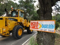FILE - Construction equipment passes a homemade sign posted in the wake of Hurricane Dorian on North Carolina's Ocracoke Island, June 25, 2020.