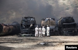 FILE - Men stand near damaged tankers of a NATO supply convoy after an attack a day earlier in Hub, about 25 km (16 miles) from Karachi, Sept. 16, 2013.