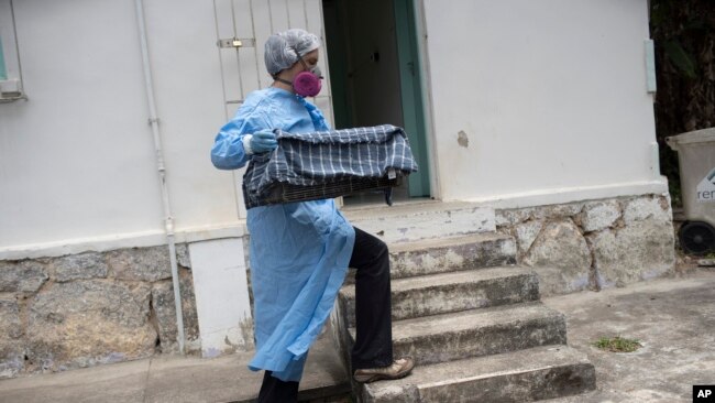 A researcher for Brazil's state-run Fiocruz Institute, wearing protective gear, transports captured monkeys to a holding area, at Pedra Branca state park, near Rio de Janeiro, Tuesday, Oct. 29, 2020. (AP Photo/Silvia Izquierdo)