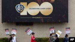 Picketers pass near a studio entrance during a Writers Guild rally outside Warner Bros. Studios, May 24, 2023, in Burbank, California.