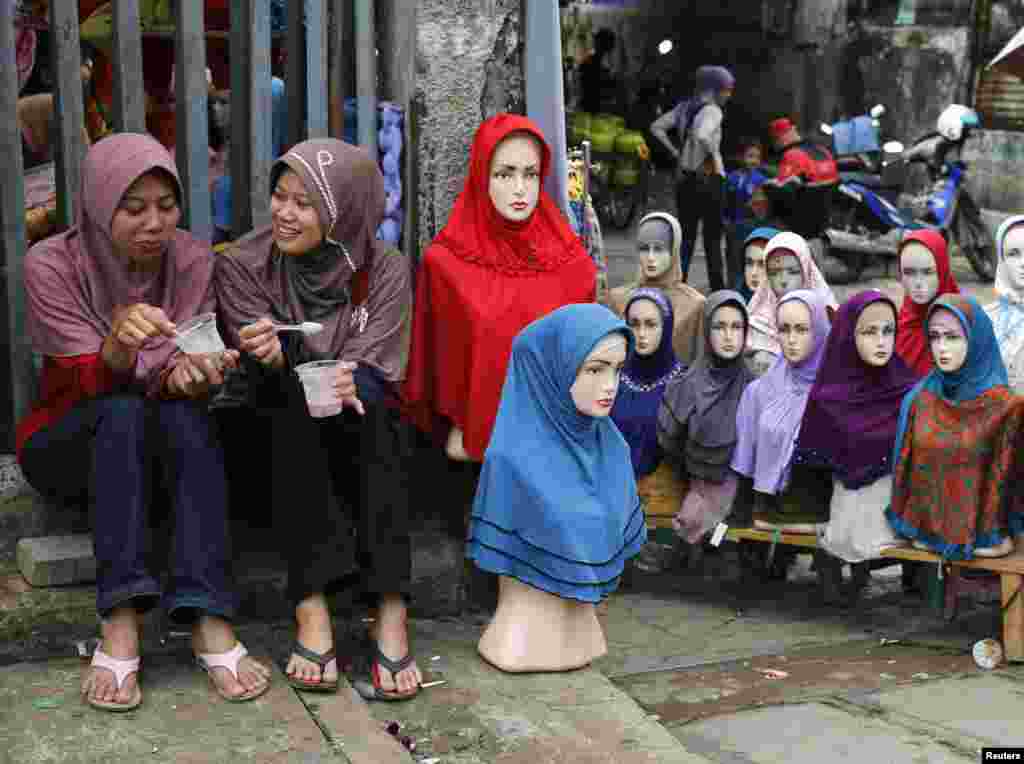 Những cô gái ngồi cạnh một hàng bán khăn trùm đầu hijab ở chợ Tanah Abang trước tháng ăn chay Ramadan, tại Jakarta, Indonesia. 