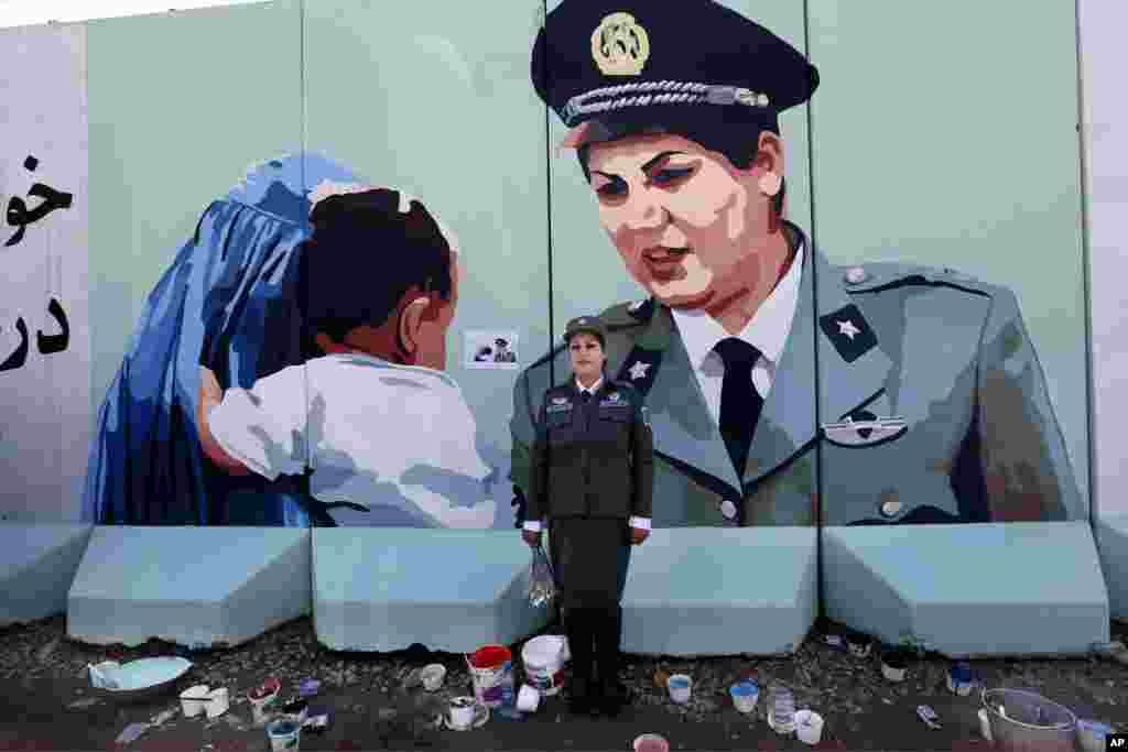 Friba Hameed, 30, an Afghan police officer, poses for a photograph in front of a mural of herself, painted by an independent artist, outside the main gate of a police precinct to mark International Women's Day in Kabul, Afghanistan, March 8, 2016. 