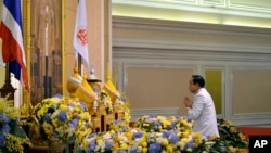 In this photo released by Thai Spokesman Office, Gen. Prayuth Chan-ocha pays a respect to a royal endorsement, black book seen at center, in front of the portrait of King Bhumibol Adulyadej as he accepted the written royal command issued by the King cert