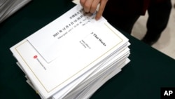 FILE - A journalist reaches for a copy of a Chinese government-produced report titled "Democracy That Works" before a press conference at the State Council Information Office in Beijing, Dec. 4, 2021. 