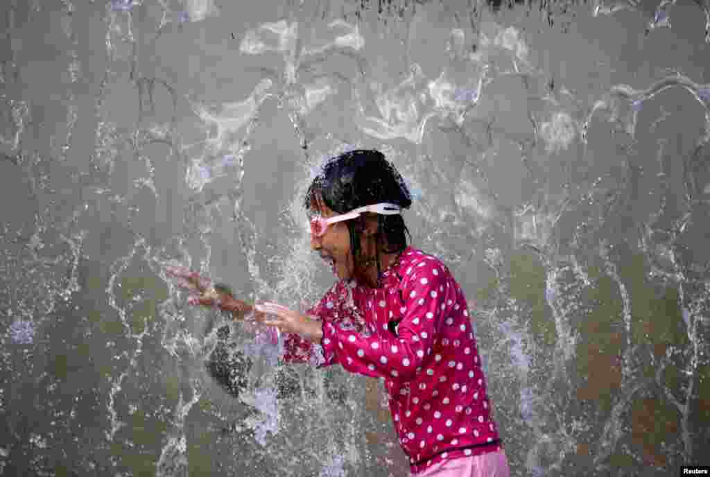 A girl plays in a fountain to cool down at a park during a hot summer day in Tokyo, Japan.