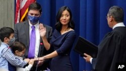 Michelle Wu raises her hand as she is sworn-in as Boston Mayor during a ceremony at Boston City Hall, Tuesday, Nov. 16, 2021, in Boston. From left with Wu are her two sons Blaise and Cass, husband Conor Pewarski and Judge Myong J. Joun. 