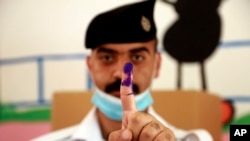 Seorang polisi Irak memamerkan jari telunjuknya yang telah dicelupkan ke tinta, tanda telah menyalurkan hak pilihnya di sebuah TPS di Baghdad, Irak, 8 Oktober 2021. ((AP Photo/Hadi Mizban)