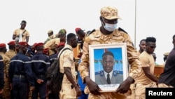 A Burkina Faso soldier holds a portrait during the Oct. 8, 2022 burial ceremony of 27 soldiers killed in an attack by Islamist militants.