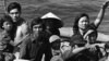 Vietnamese refugees wait to be taken aboard the amphibious command ship USS BLUE RIDGE in 1984. 