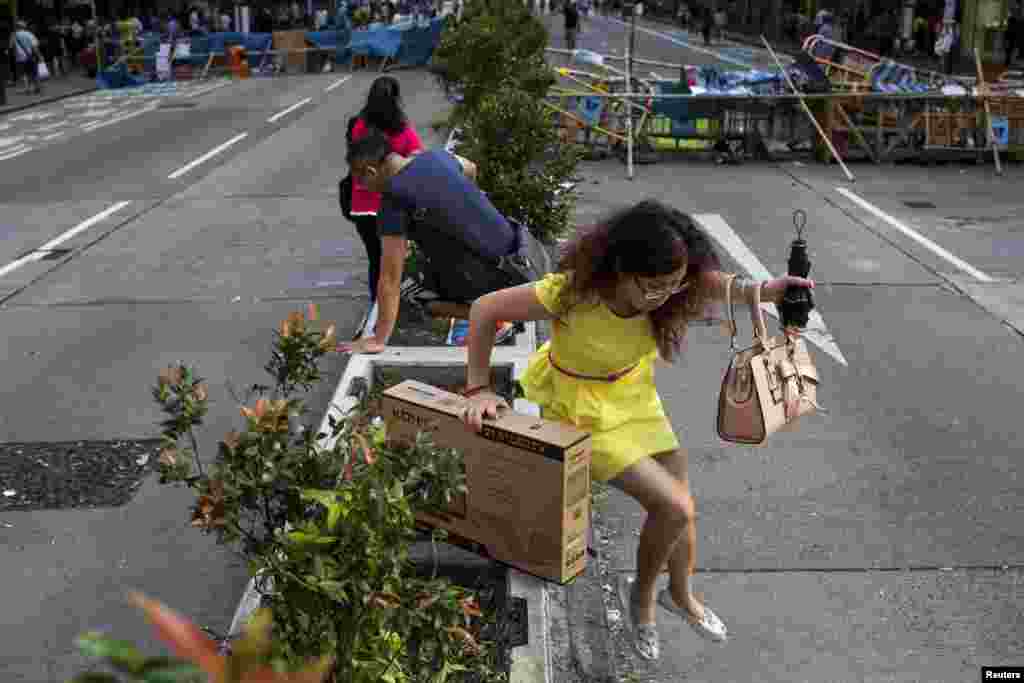 A mainland Chinese visitor jumps over a planter as she crosses a road blocked by the Occupy Central movement protesters on the Mong Kok shopping district in Hong Kong, Oct. 6, 2014.