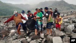 Rescuers and villagers carry a body bag containing the remains of a victim in the eruption of Mount Semeru, in Candi Puro village, Lumajang, East Java, Indonesia, Dec. 7, 2021. 