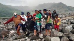 Tim SAR dan warga desa membawa kantong yang berisi jenazah korban letusan Gunung Semeru, dalam proses evakuasi di Candi Puro, Lumajang, Jawa Timur, pada 7 Desember 2021. (Foto: AP)