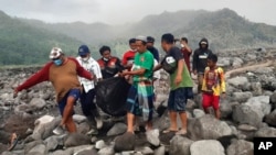 Tim SAR dan warga desa membawa kantong yang berisi jenazah korban letusan Gunung Semeru, dalam proses evakuasi di Candi Puro, Lumajang, Jawa Timur, pada 7 Desember 2021. (Foto: AP)
