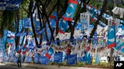 Seorang warga Malaysia berjalan melewati poster dan bendera kampanye dari kedua partai yang saling bersaing dalam pemilu Minggu mendatang - partai Barisan Nasional yang berkuasa dan partai oposisi Keadilan Rakyat - yang menghiasi sisi sebuah jalan di Malaysia menjelang pemilu (1/5).