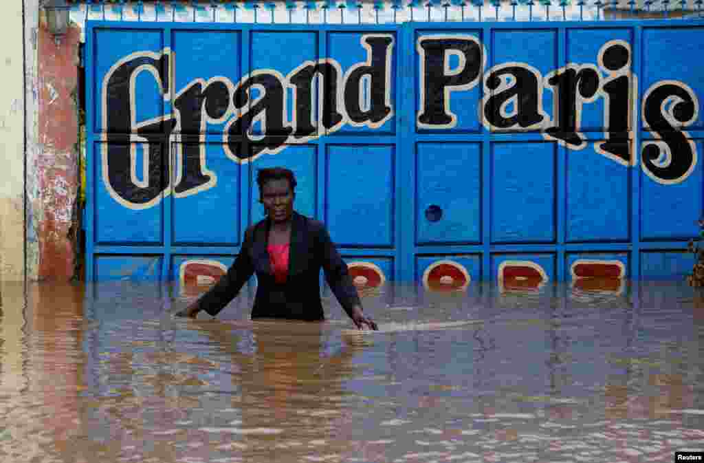 A trader wades through a flooded street outside her premises after the River Nzoia burst its banks due to a backflow from Lake Victoria, in Nyadorera, Siaya County, Kenya, May 2, 2020.