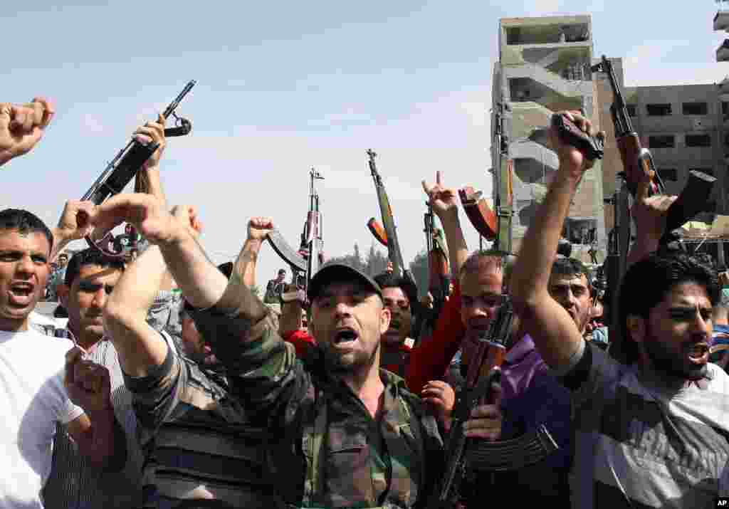 Syrian security officers shout slogans in front of a damaged military intelligence building where two bombs exploded.
